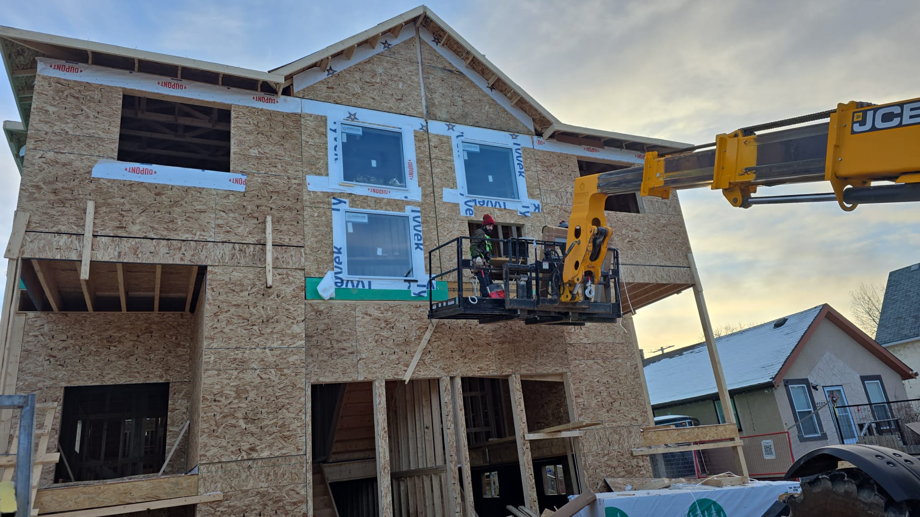 Three-storey residential build with OSB sheathing, house wrap and new windows, crew working from a telehandler lift in Calgary
