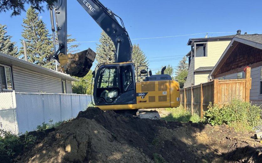 Tracked excavator digging out a residential lot, with a mound of excavated soil and an open pit