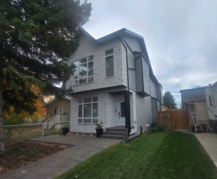 Completed two-storey home with light brick, dark trim and a covered front entry on a finished lawn