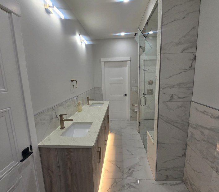 Bathroom renovation by HDL Construction with a light wood double vanity and marble-look tile