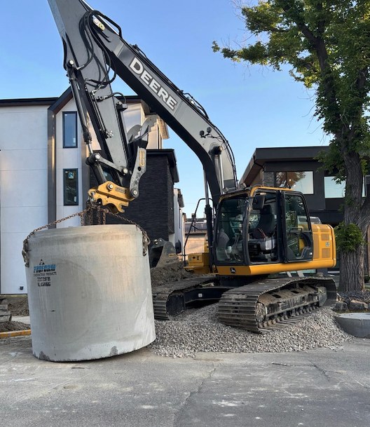 Excavator setting a concrete drainage structure on a residential job site